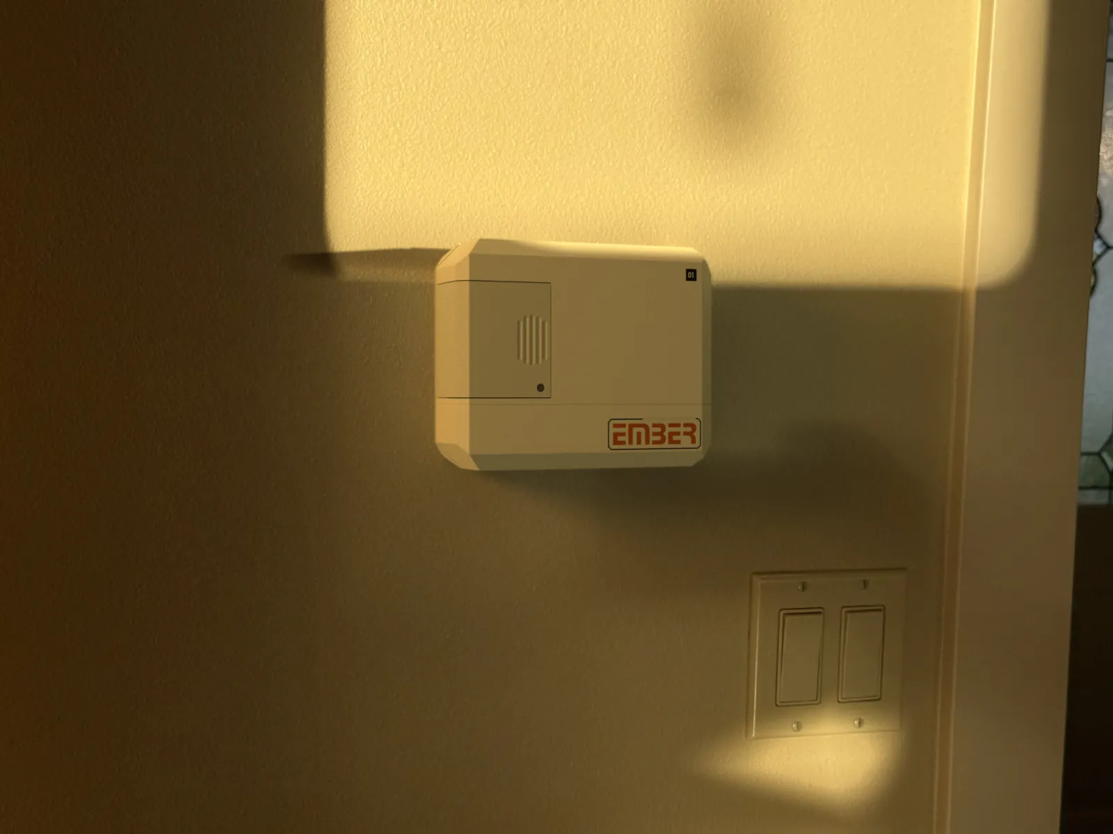 Photo of the wall from further back, with the Ember render on the thermostat and a light switch below it.